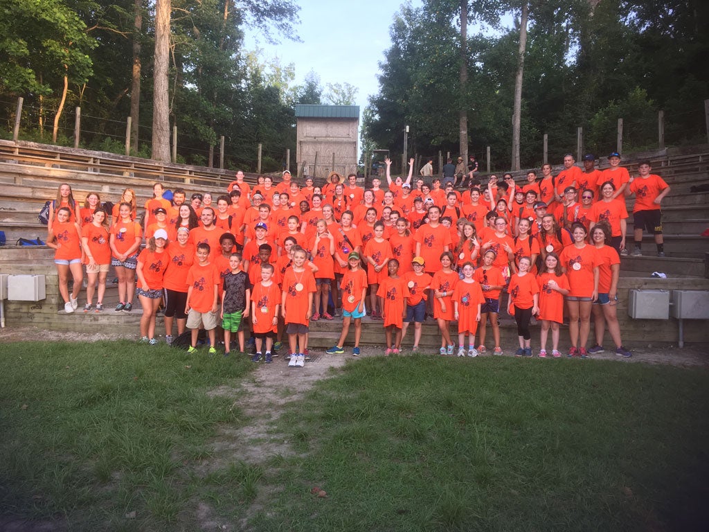 A group of campers wearing bright orange t-shirts standing in an amphitheater.